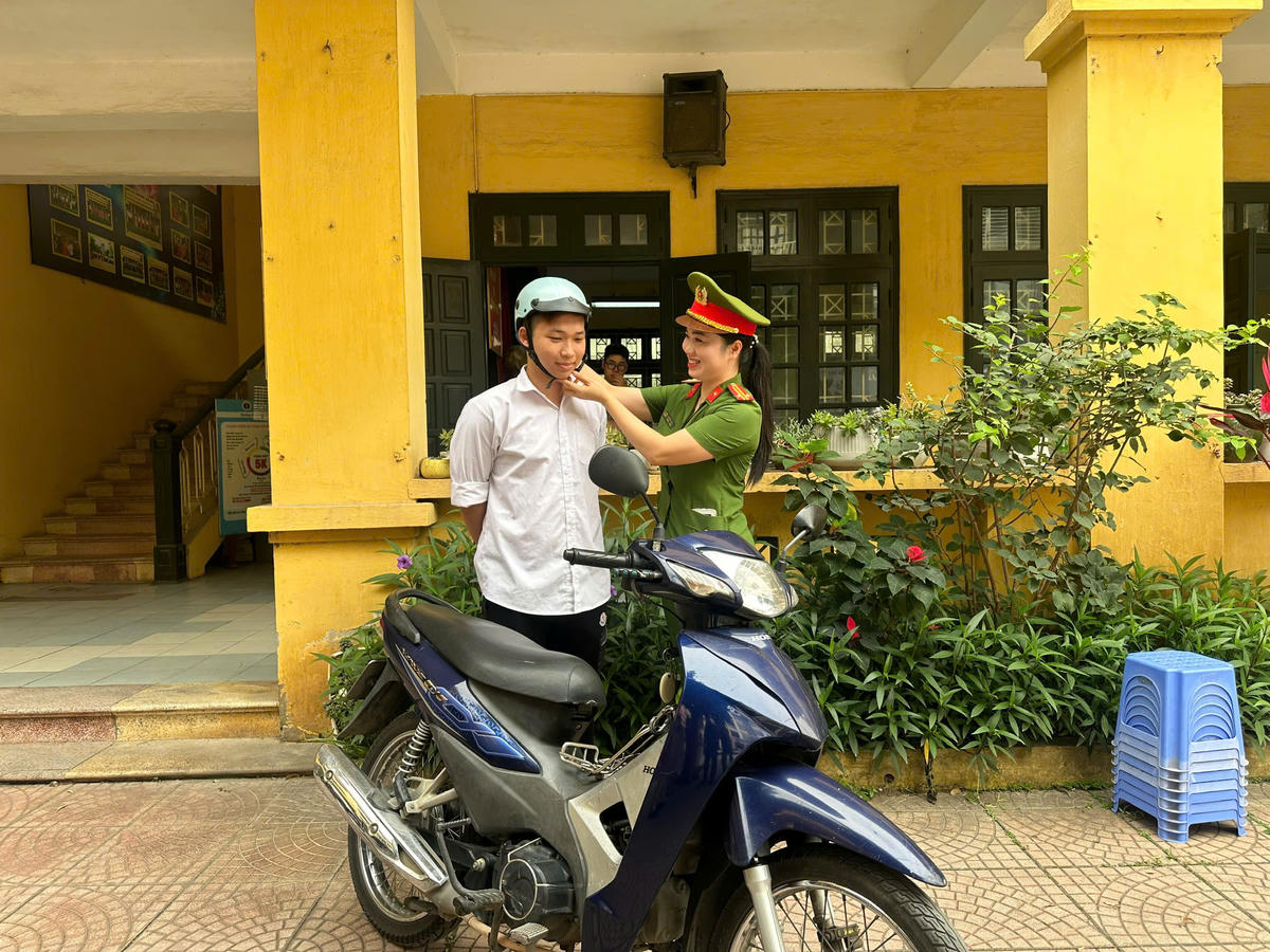 Trung tá Hà Hồng Nhật hướng dẫn học sinh đội mũ bảo hiểm đúng quy định.